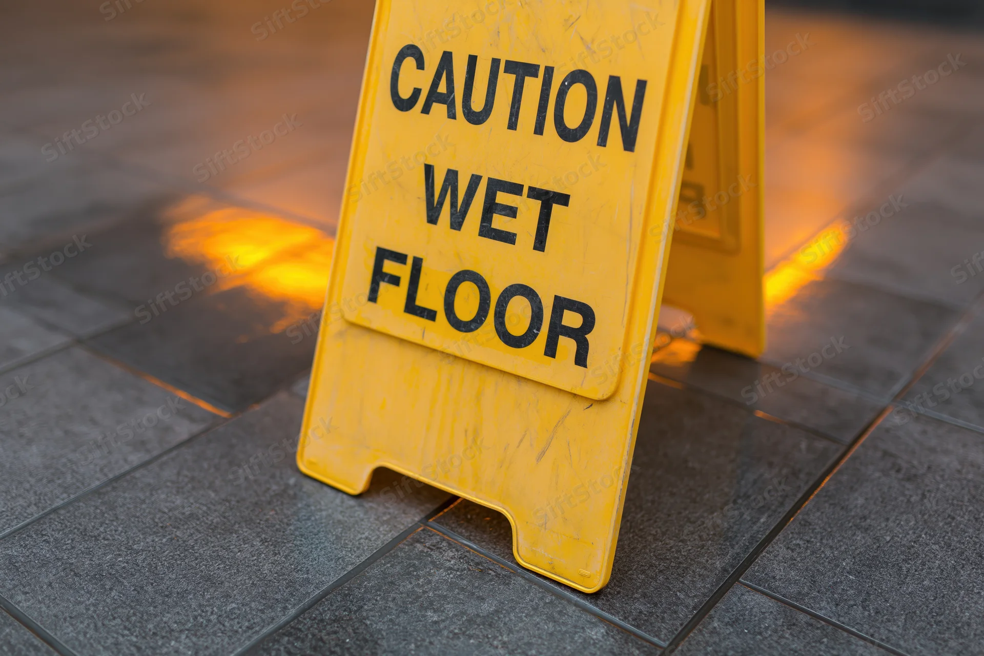 Yellow plastic caution wet floor a-frame sign standing on tiled floor with reflective light