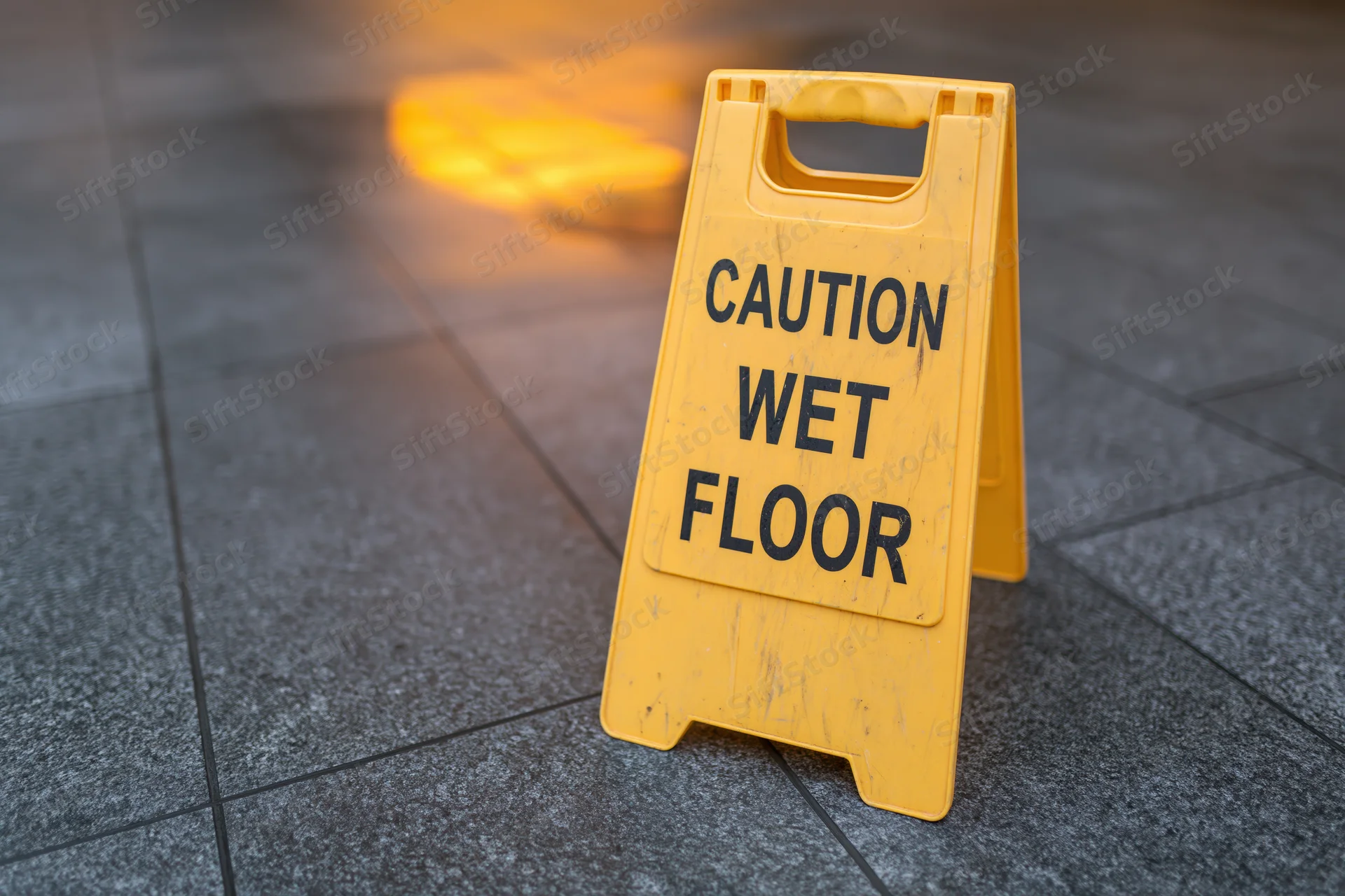 Yellow plastic caution wet floor aframe sign standing on gray tiled floor at night under artificial light