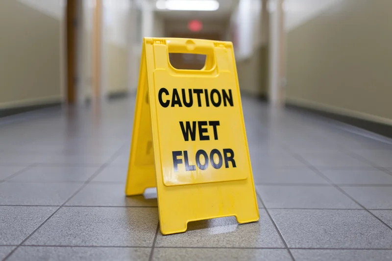 Yellow plastic folding caution wet floor sign placed on tiled hallway floor