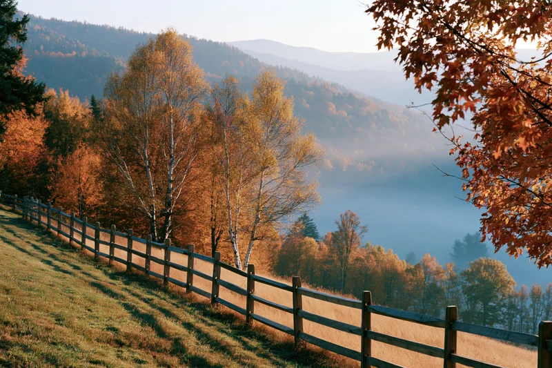 Autumn hillside landscape with wooden split-rail fence running along grassy slope overlooking misty valley and forested mountains