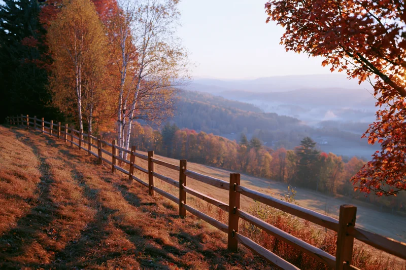 Autumn hillside landscape with wooden split-rail fence running along grassy slope overlooking misty valley