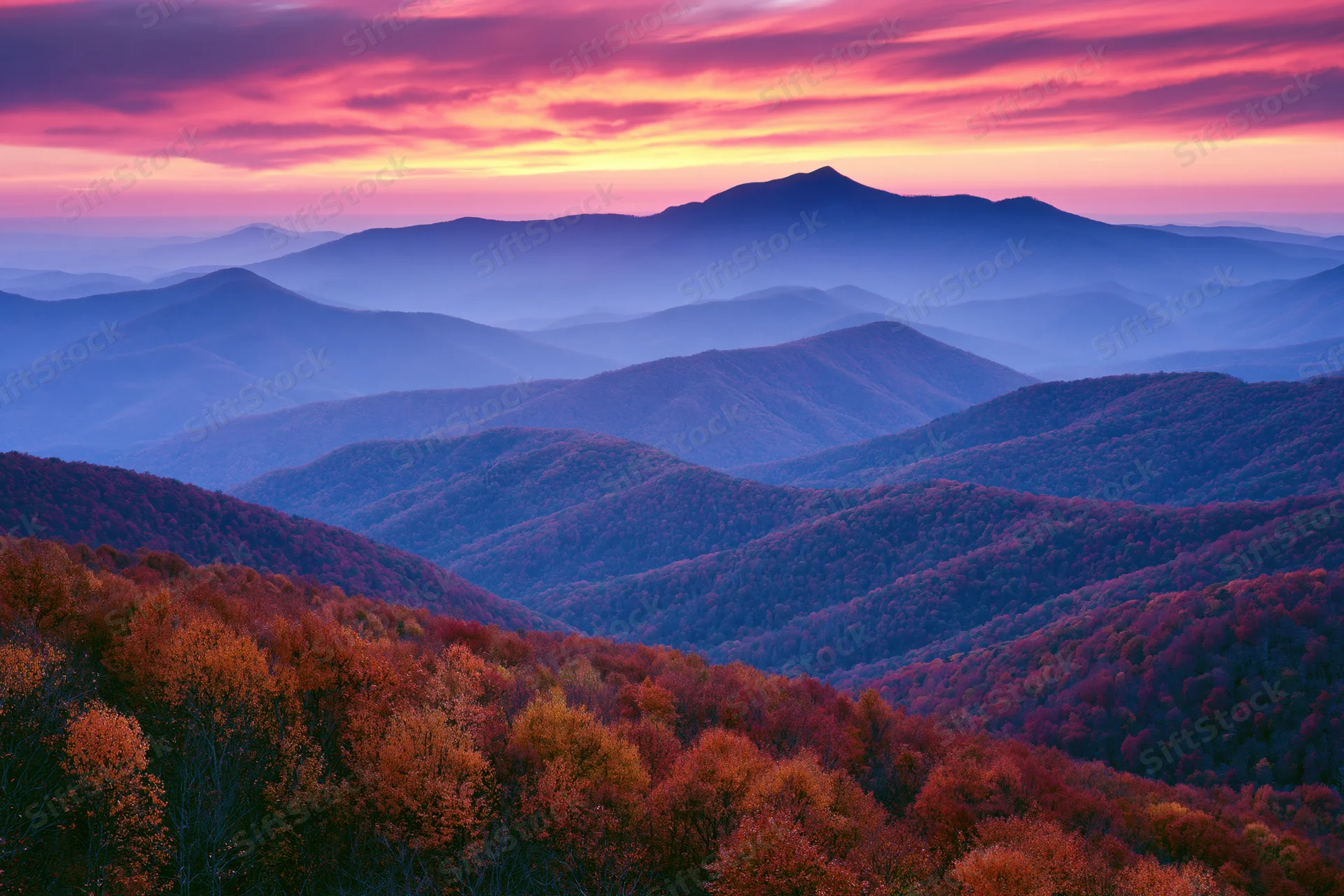 Rolling forested mountains under a colorful sunset sky in autumn