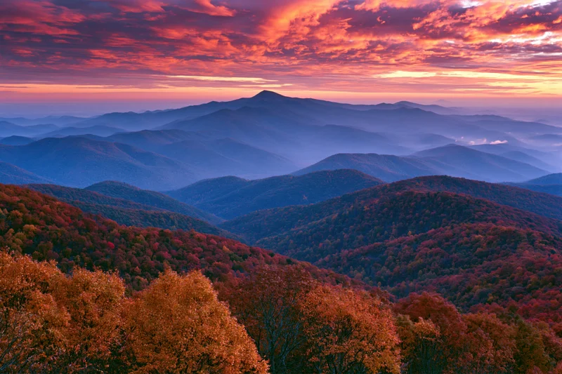 Rolling mountains covered in autumn foliage under a fiery sunset sky