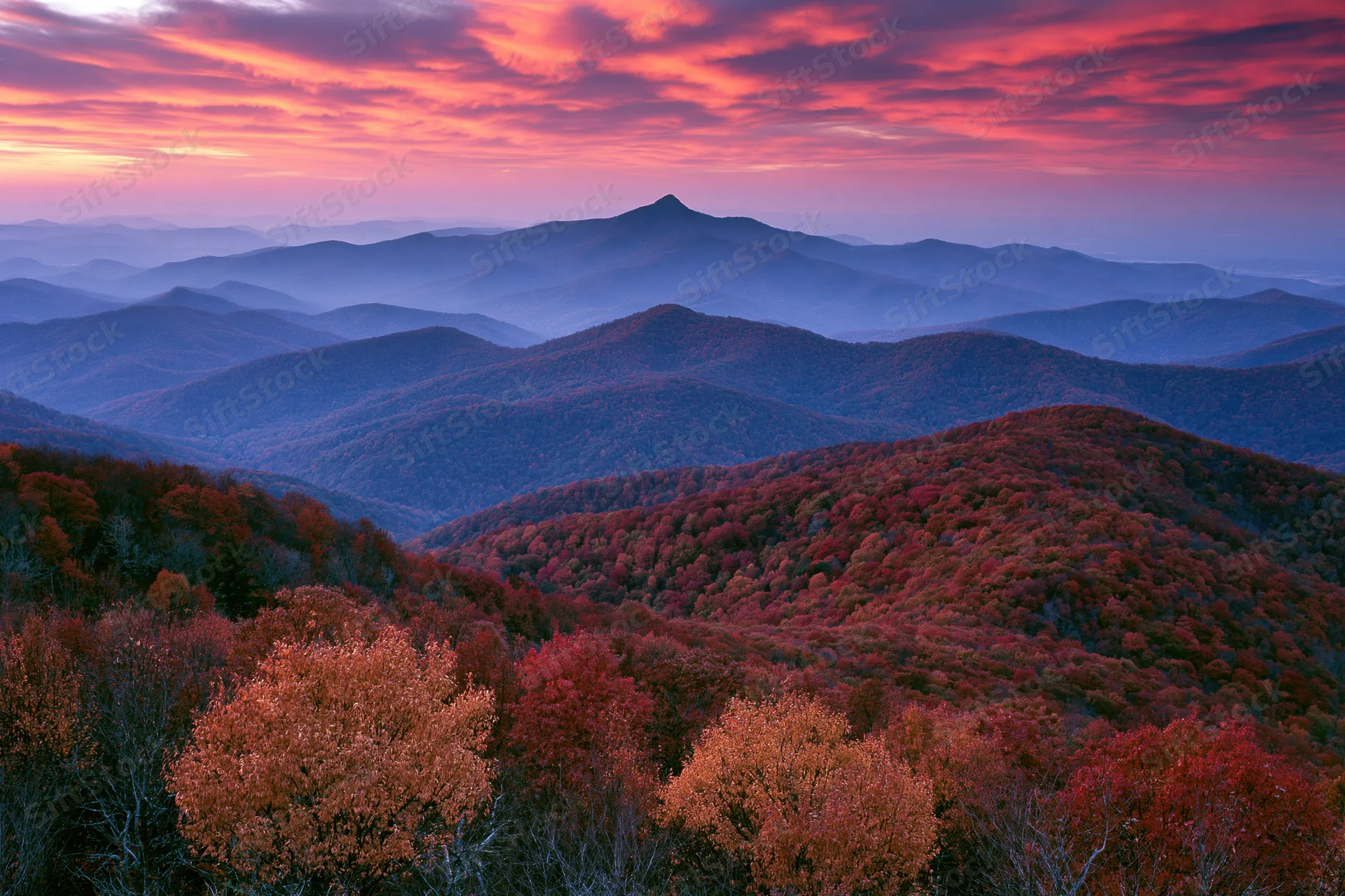 Rolling mountains covered in autumn foliage under a colorful sunset sky