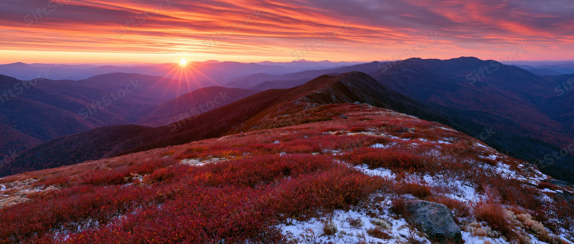 Mountain ridge covered in red autumn foliage at sunset with layered ridges and colorful sky