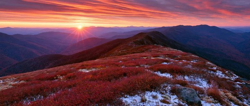 Mountain ridge covered in red autumn foliage at sunset with layered ridges and colorful sky