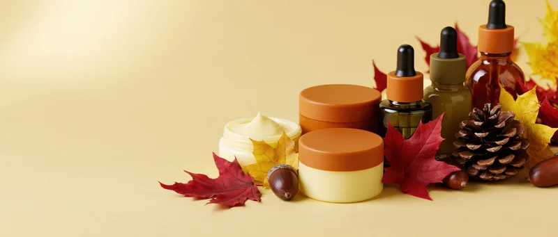 Autumn skincare products arranged with leaves and pinecones on a warm beige background
