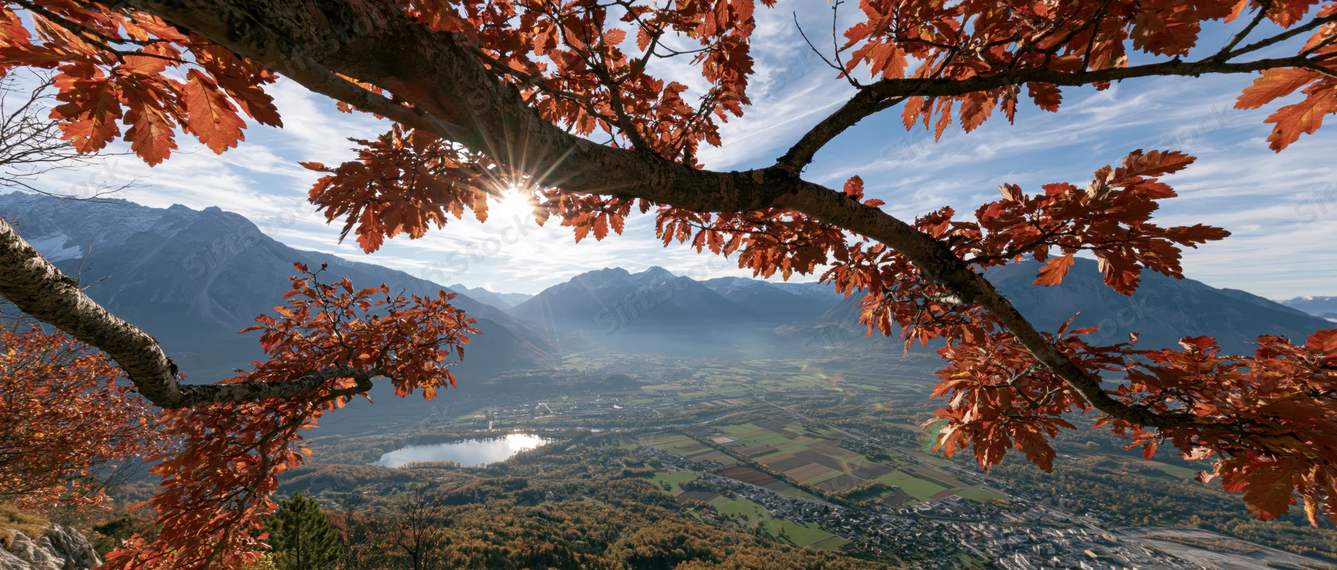 Autumn tree branches with orange-red leaves framing a mountain valley view