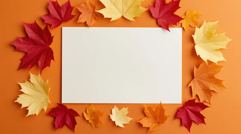Blank white card surrounded by colorful maple leaves arranged in a border on orange background