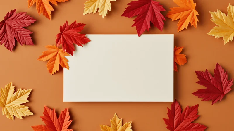Blank cream-white card centered on orange surface surrounded by colorful autumn maple leaves in flat lay arrangement