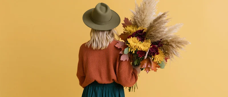 Woman from behind holding large autumn bouquet of dried pampas grass and colorful flowers against yellow background