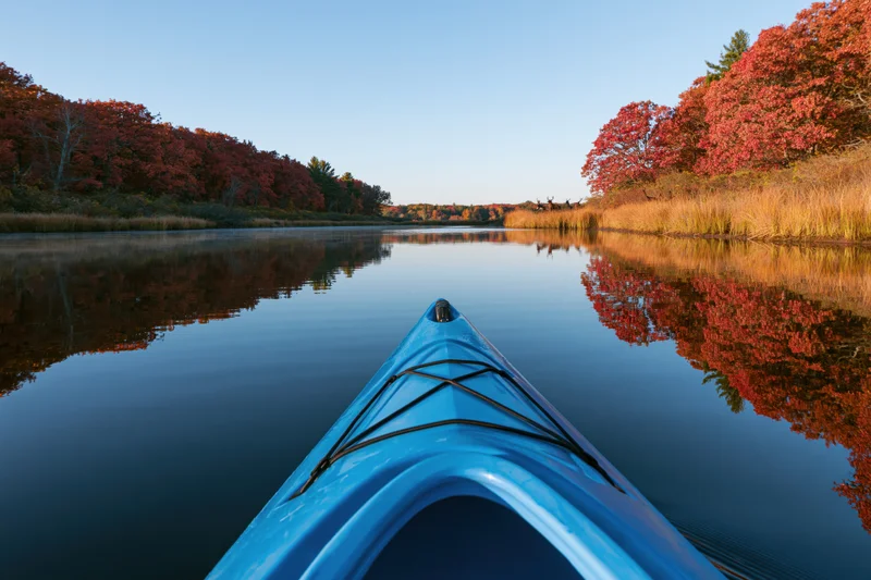 Blue kayak bow pointing forward on calm river surrounded by autumn trees reflecting in still water