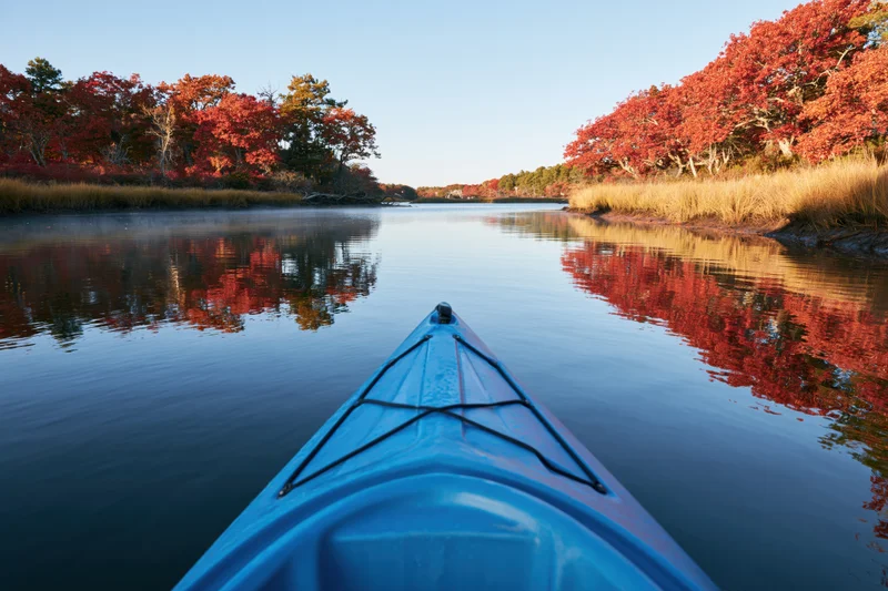Blue kayak bow gliding on calm river flanked by red autumn trees reflecting in water