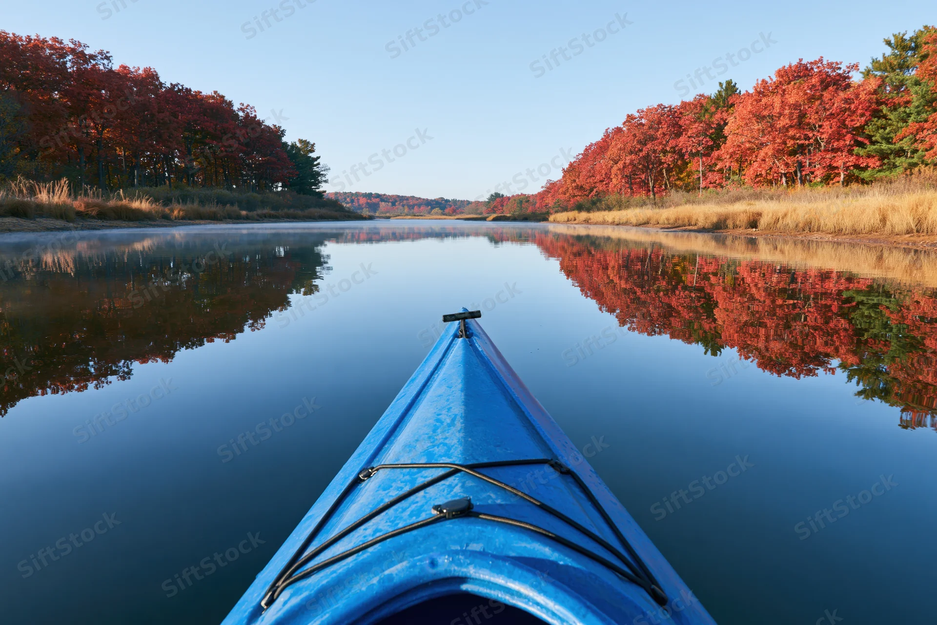 Blue kayak bow pointing forward on calm river surrounded by autumn trees reflecting in water