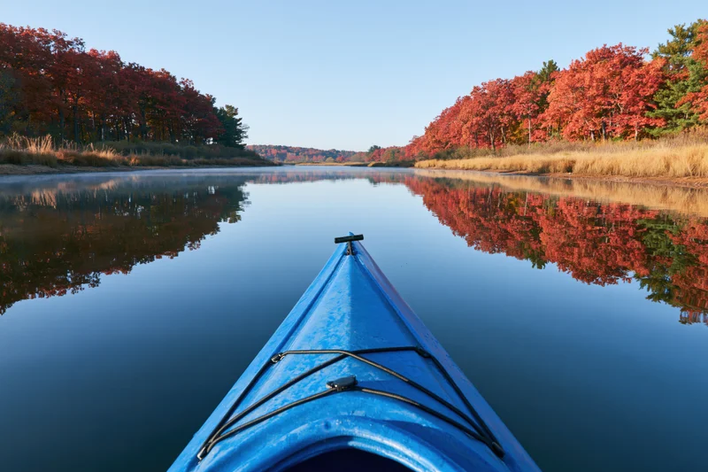 Blue kayak bow pointing forward on calm river surrounded by autumn trees reflecting in water