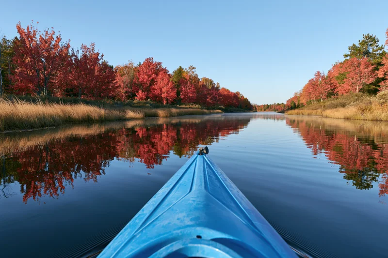 Blue kayak bow gliding on calm river surrounded by autumn trees reflecting in water