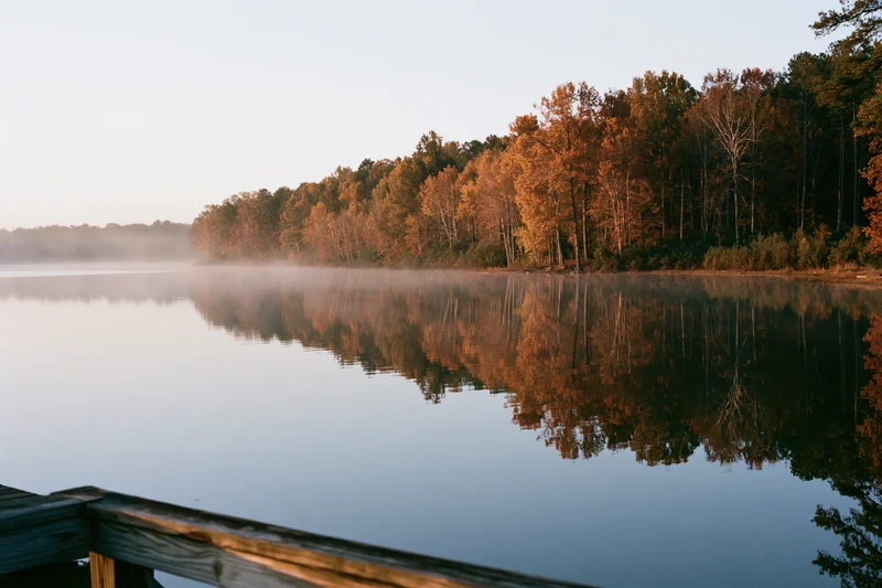 Calm lake reflecting autumn trees in orange amber light at dawn near a wooden dock