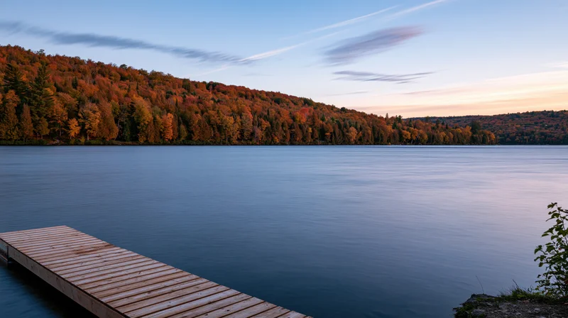 Wooden dock extending over calm lake at dusk surrounded by autumn forest