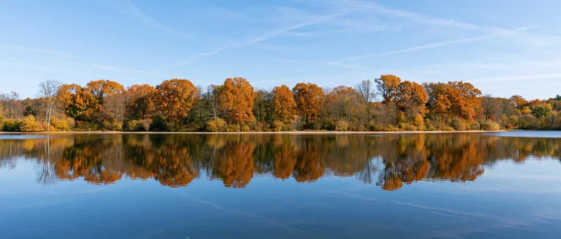 Calm lake reflecting autumn trees along the shoreline under a clear blue sky