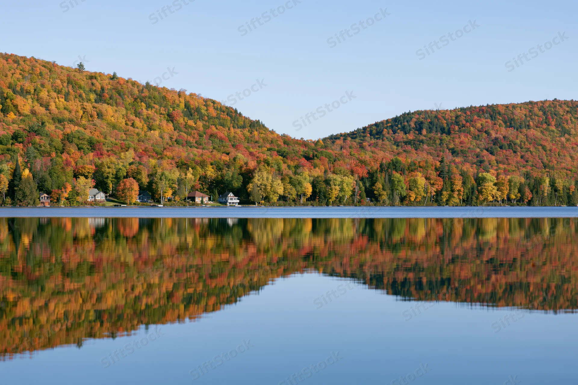Calm lake reflecting twin forested hills covered in peak autumn foliage