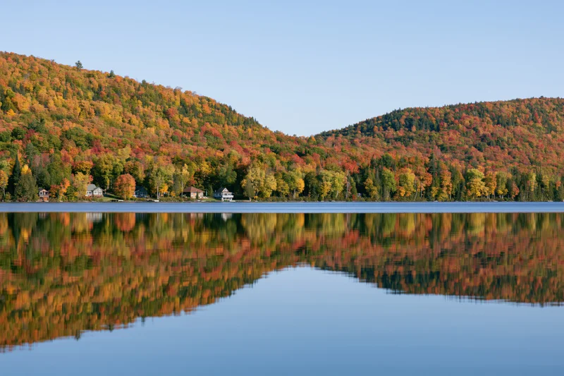 Calm lake reflecting twin forested hills covered in peak autumn foliage