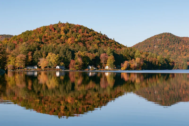 Calm lake reflecting forested hills covered in autumn foliage under clear sky