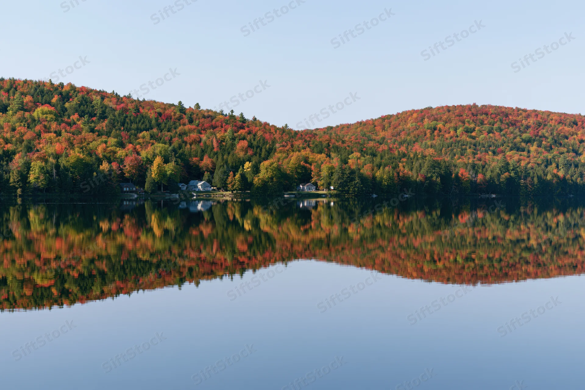 Calm lake reflecting twin forested hills covered in peak autumn foliage