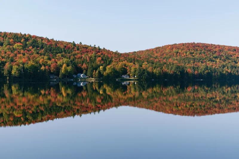 Calm lake reflecting twin forested hills covered in peak autumn foliage
