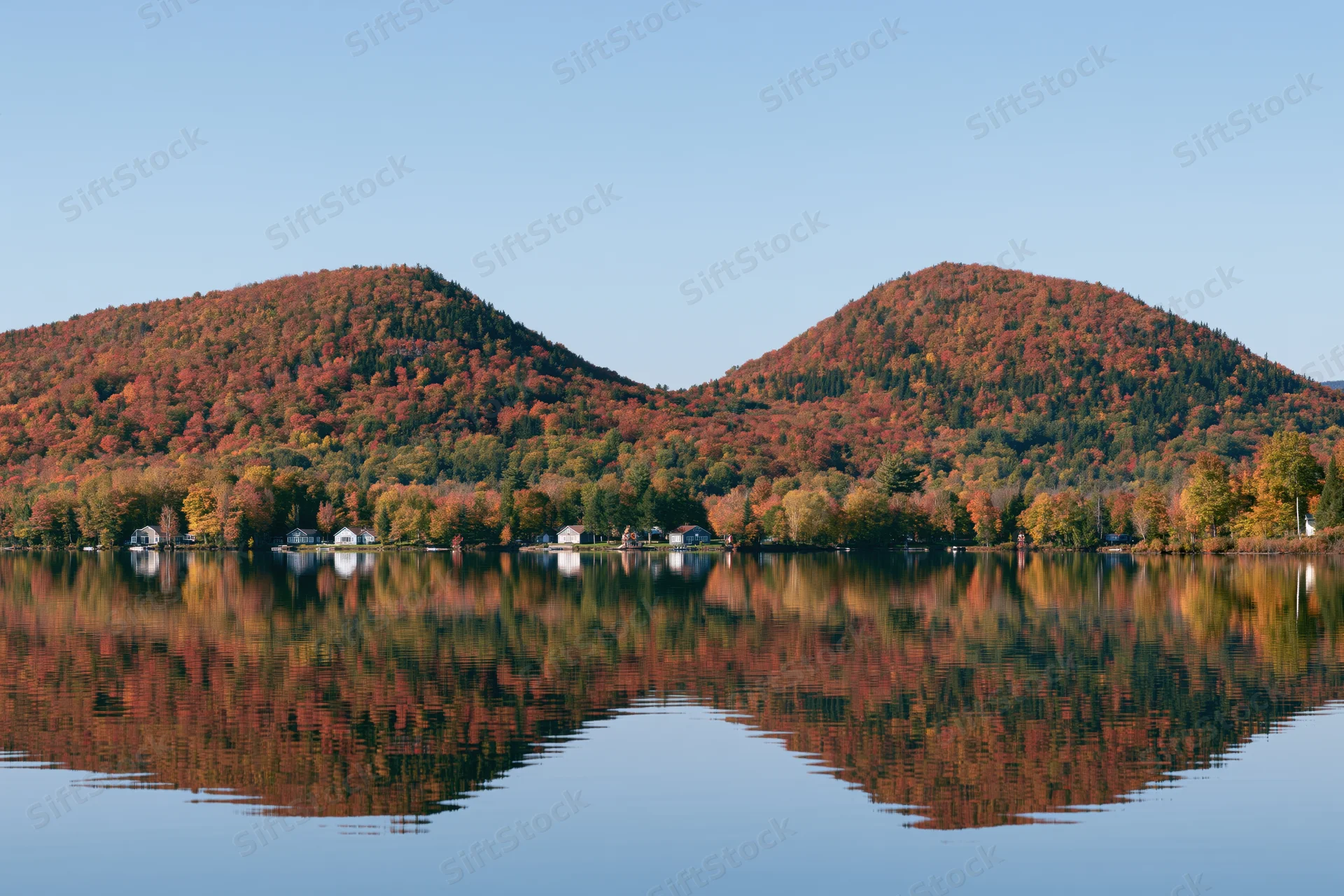 Calm lake reflecting twin forested hills covered in peak autumn foliage