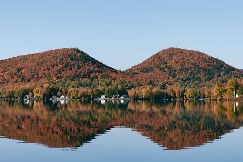 Calm lake reflecting twin forested hills covered in peak autumn foliage