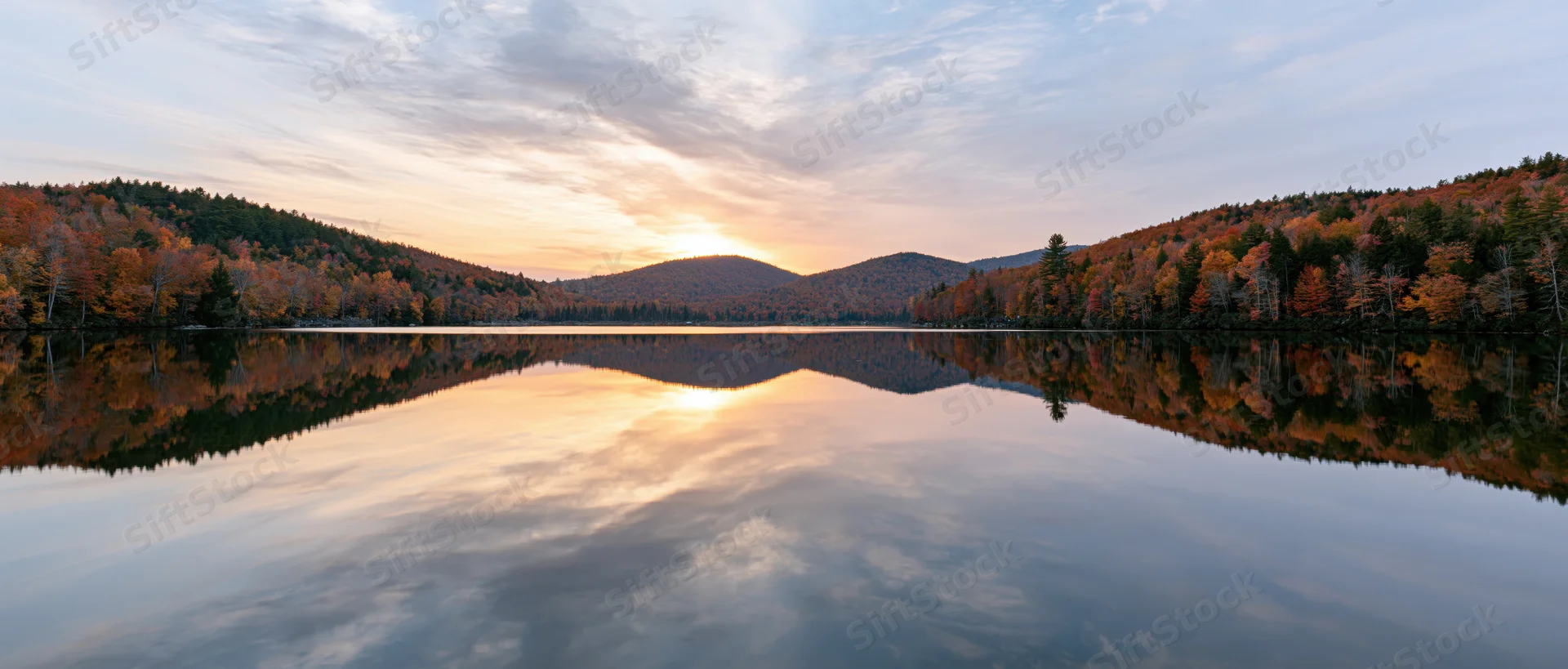 Calm mountain lake reflecting autumn foliage hills at sunset