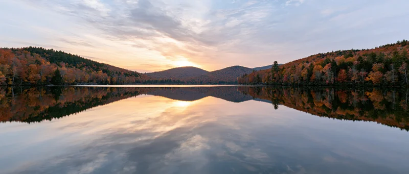 Calm mountain lake reflecting autumn foliage hills at sunset