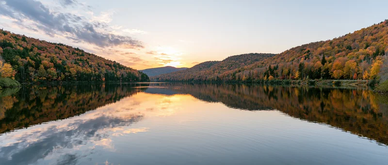 Calm mountain lake reflecting autumn foliage hills at sunset
