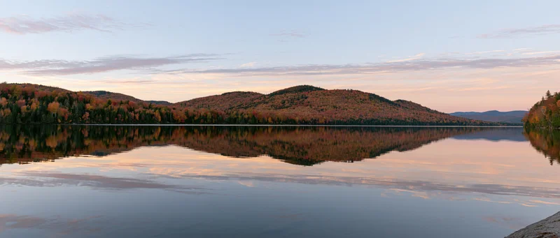 Calm mountain lake reflecting autumn foliage hills at sunset