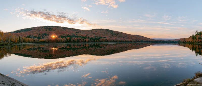 Calm mountain lake reflecting autumn foliage hills at sunset