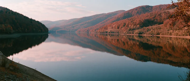 Calm mountain lake reflecting autumn forest and hillsides at dusk