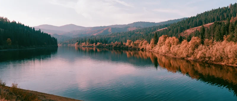 Calm mountain lake reflecting autumn forest and hillsides at dusk