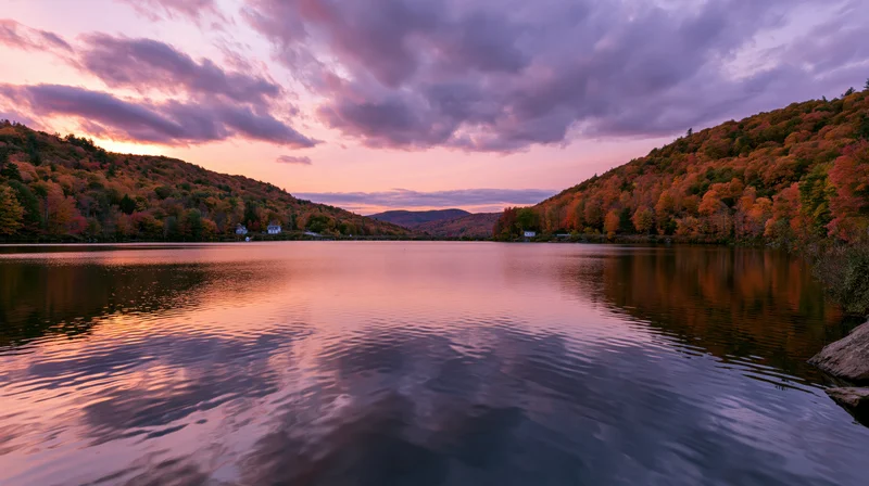 Calm mountain lake reflecting autumn forest hillsides at sunset