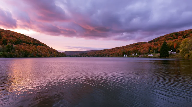 Calm mountain lake reflecting autumn forest hillsides at sunset