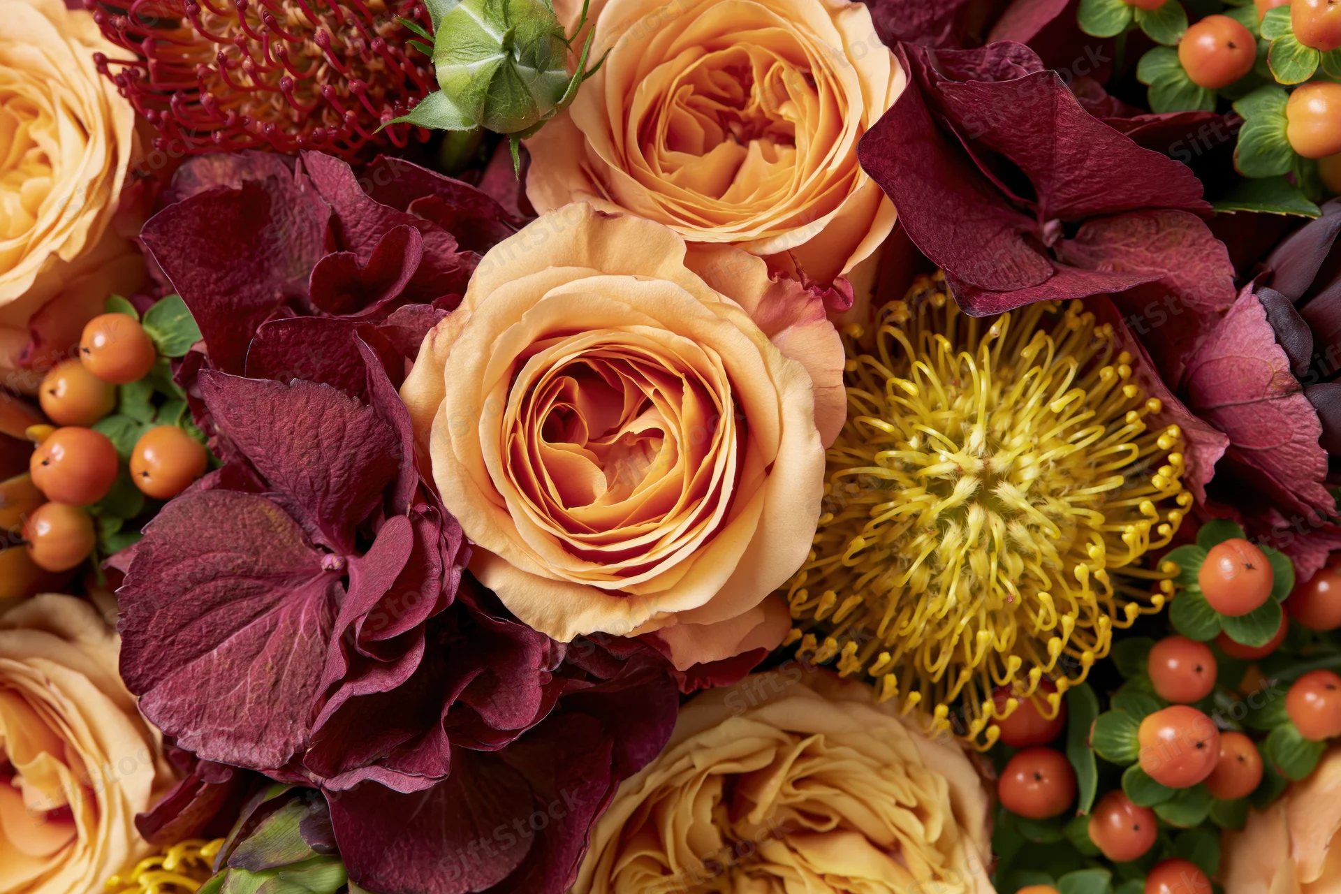Close-up flat lay of an autumn floral arrangement with roses, hydrangea, and hypericum berries filling the frame