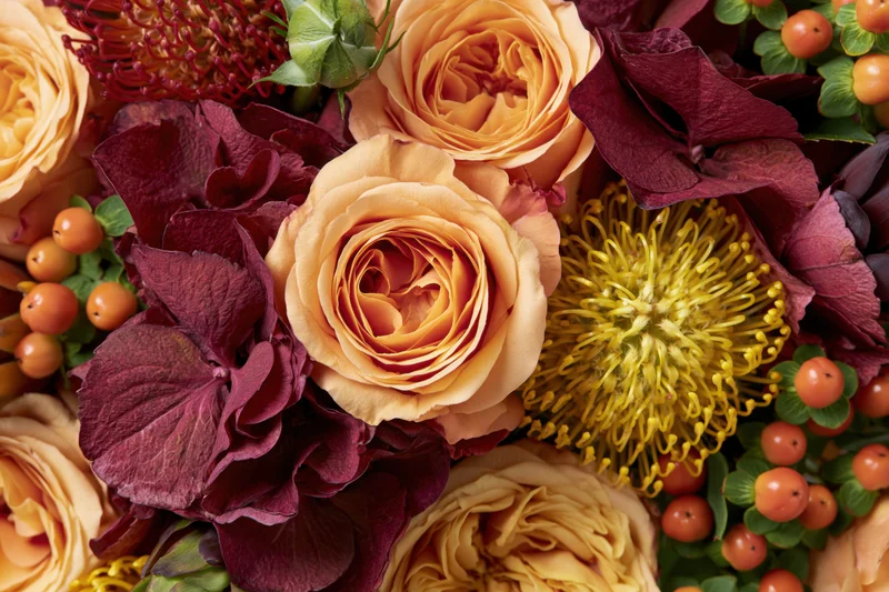 Close-up flat lay of an autumn floral arrangement with roses, hydrangea, and hypericum berries filling the frame