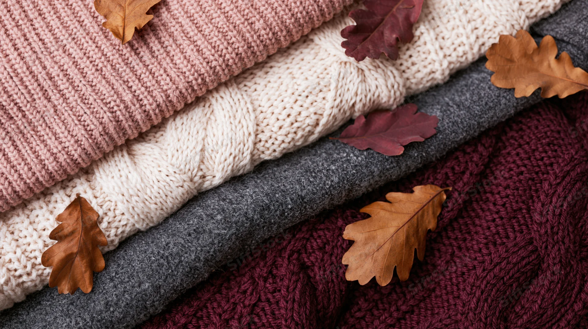 Folded knit sweaters stacked with autumn leaves on flat surface