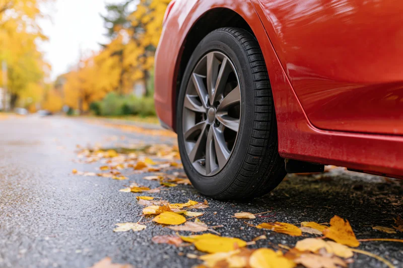 Red sedan front wheel on pavement with fallen autumn leaves