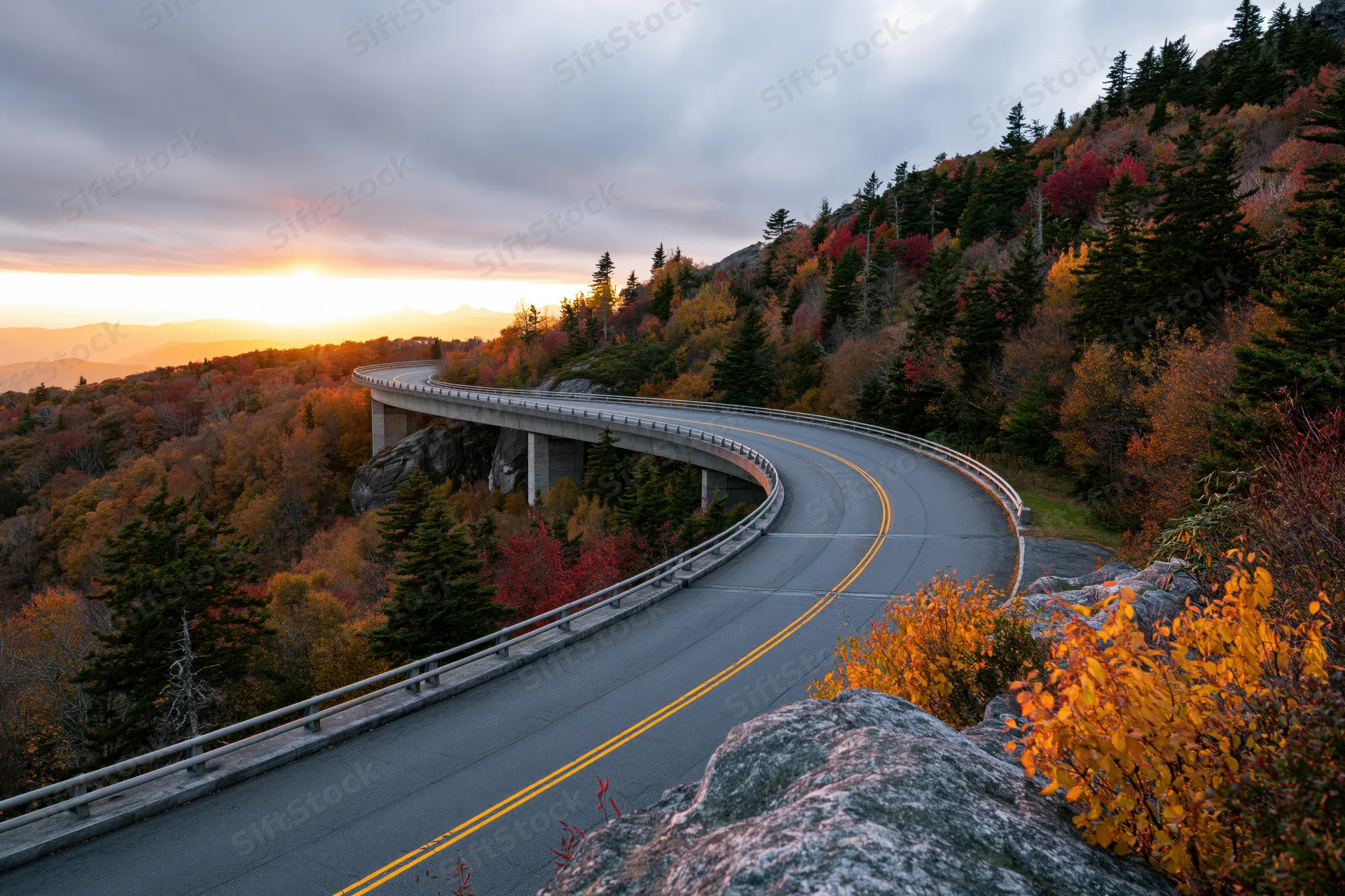 Curved concrete viaduct highway winding through autumn forested mountains at sunset