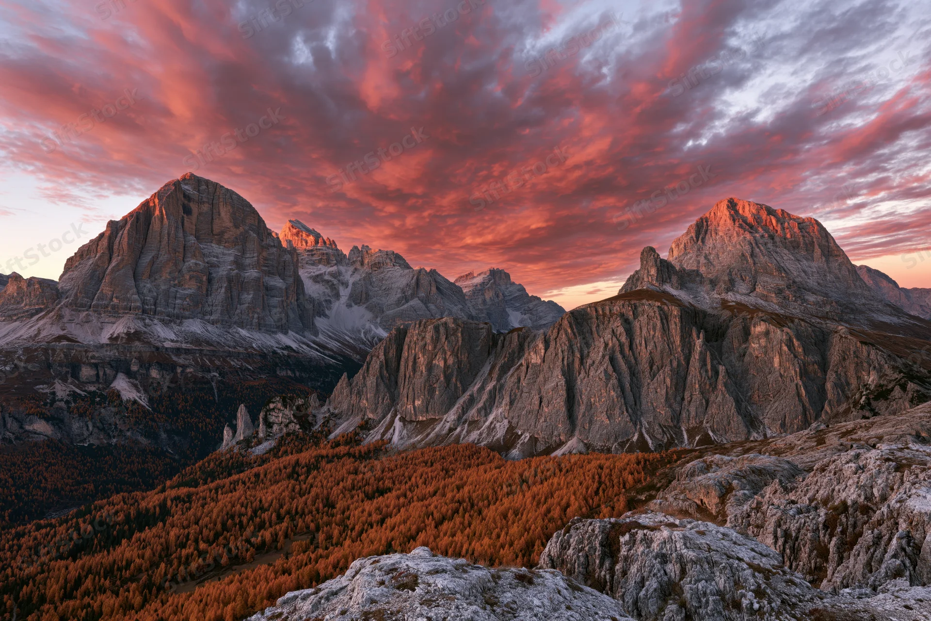 Massive limestone peaks of the dolomites at sunset with autumn forest below