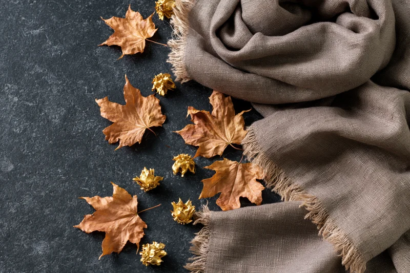 Dried maple leaves and golden seed pods arranged with a gray scarf on a dark stone surface