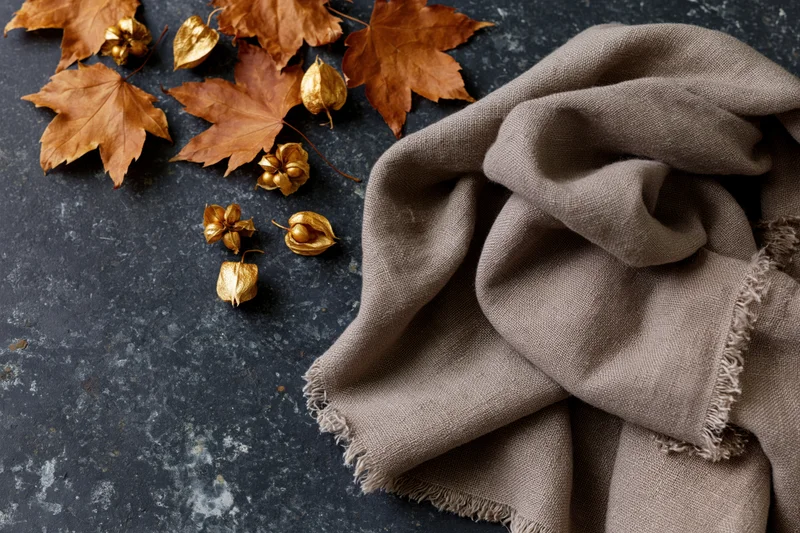 Dried maple leaves and golden seed pods arranged with a brown scarf on a dark stone surface