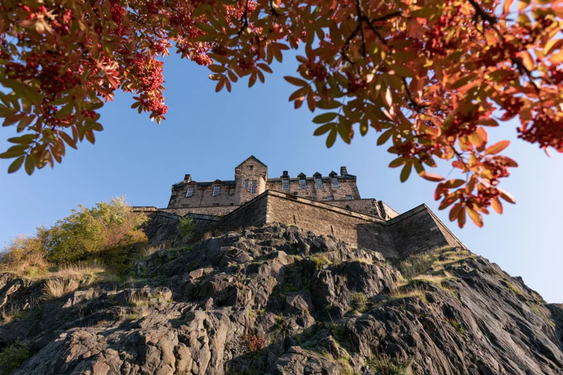 Edinburgh castle perched on volcanic rock viewed from below through autumn foliage