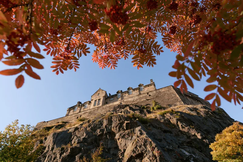 Edinburgh castle perched on volcanic rock viewed from below through autumn leaves