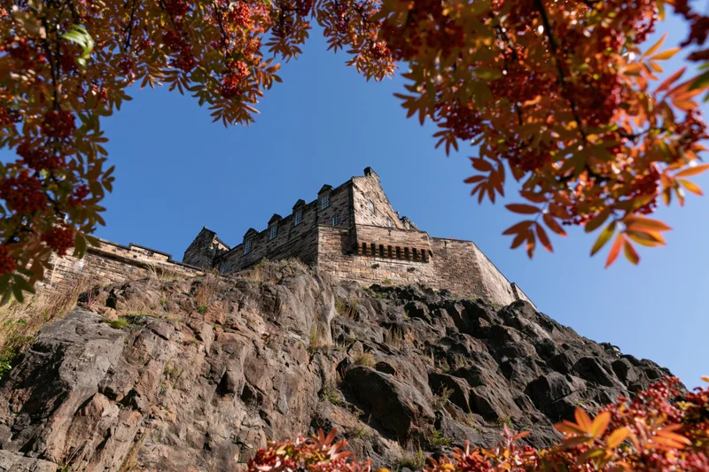 Edinburgh castle perched on volcanic rock viewed from below through autumn foliage